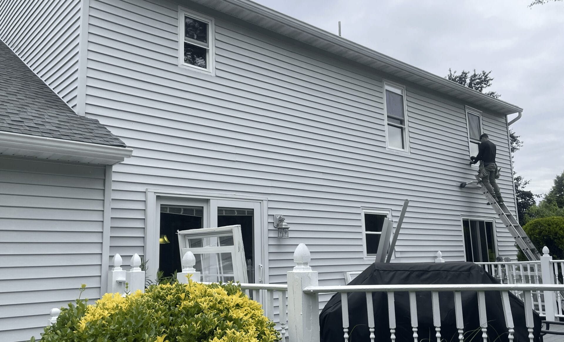 A professional cleans the exterior of a vinyl window while standing on a ladder.
